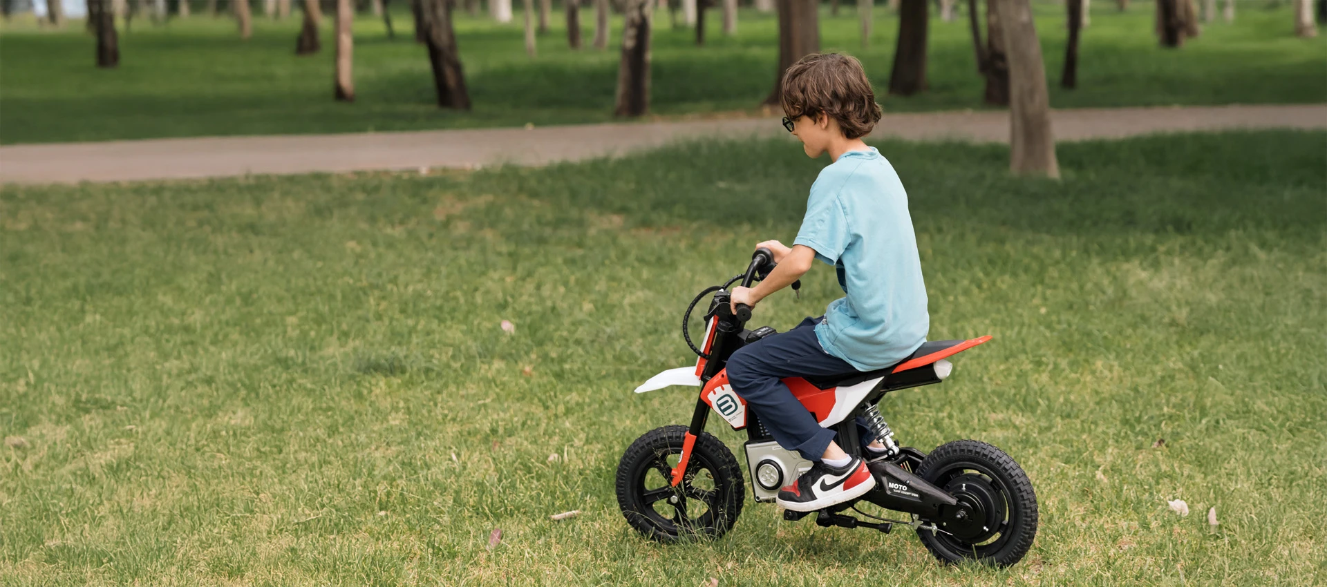 Niño usando motocicleta eléctrica infantil sobre pasto en un parque